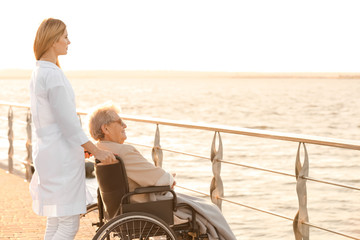 Young nurse from care home and senior woman in wheelchair near river