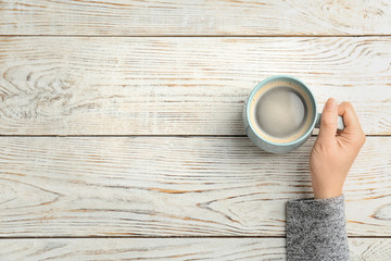 Young woman with cup of delicious hot coffee on wooden background, top view