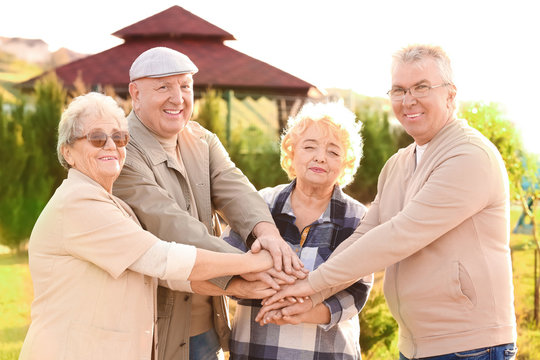 Senior people from care home putting hands together as symbol of unity outdoors