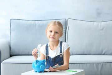 Little girl putting money into piggy-bank indoors