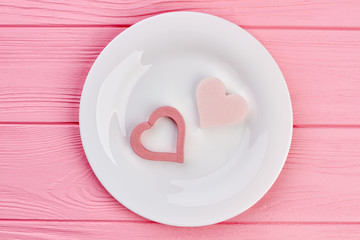 Decorative hearts on white plate, top view. Two pink hearts on plate, pink wooden background. Love and romance concept.