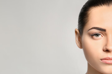 Young woman with permanent eyebrows makeup on grey background