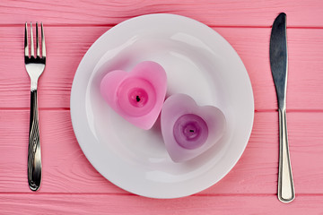 Romantic table setting, top view. Two heart shaped candles on white plate. Knife and fork on pink wood. Happy Valentines Day.