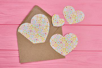 Open envelope and paper hearts. Vintage style envelope and paper hearts on pink wooden background. Love letter concept.