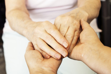 Mature female in elderly care facility gets help from hospital personnel nurse. Senior woman w/ aged wrinkled skin & care giver, hands close up. Grand mother everyday life. Background, copy space.