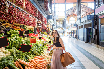 Fototapeta premium Young woman choosing goods standing at the counter with a bunch of different fresh food in theGreat Market hall in Budapest