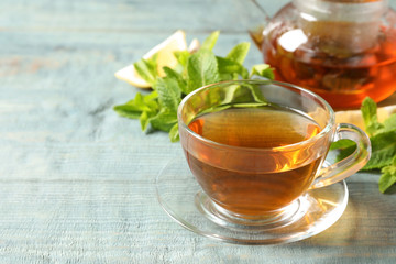 Cup with hot aromatic mint tea and fresh leaves on table