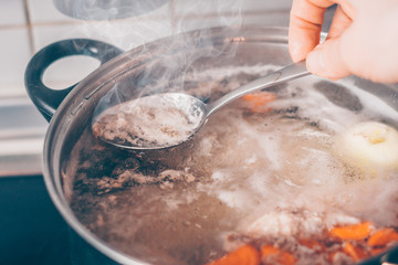 Cook with a spoon removes the foam from the boiling soup in a saucepan