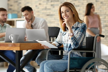 Young woman in wheelchair and colleagues at workplace