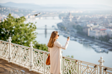 Young woman photographing beautiful morning view on Budapest city from the Gellert hill in Hungary