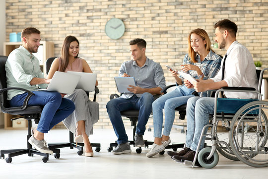 Young man in wheelchair with colleagues at workplace