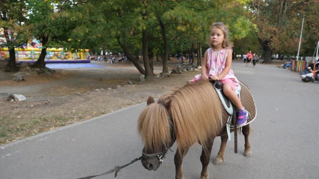 Cute smile face kid girl enjoy ride a pony horse in park in Sofia Bulgaria