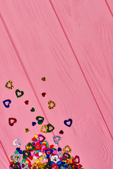 Glitter paper hearts and copy space. Collection of multicolored shiny heart shaped confetti on pink background, top view. Festive party decoration.