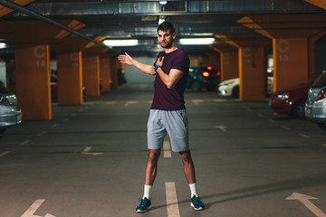 Young male runner stretching his muscles before workout in the underground car parking.