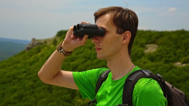 Expert explorer in the jungle looking away through binoculars.