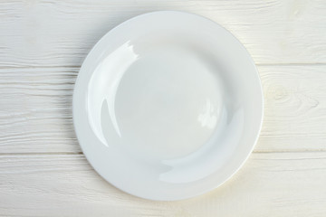 Top view of white empty plate. Ceramic plate on white wooden background.