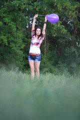 Young woman with dark curly hair. A young woman is jumping barefoot on the grass. A young woman is jumping with a balloon in her hand.