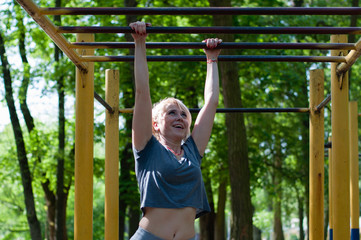 Obraz premium A young fitness woman is playing sports on a sports field in a park on a sunny summer afternoon. A girl shakes a press, stretches, walks along the stitch