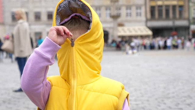 Little kid girl have fun playfuly hiding closing a zipper of yellow sleeveless jacket with a hood