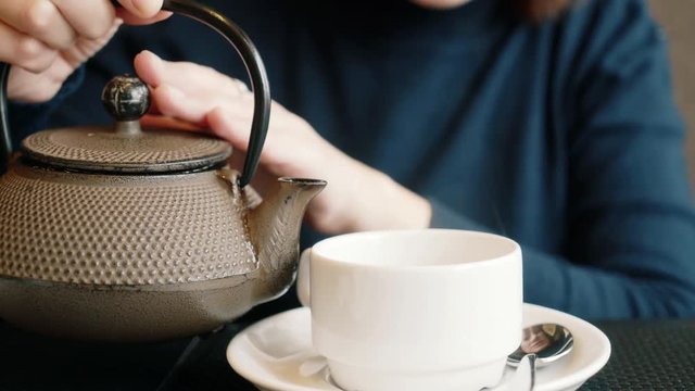 The girl pours the tea into a cup. A woman spills tea from a teapot.