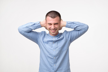 Stressed frustrated young man plugging his ears and keeping eyes closed.