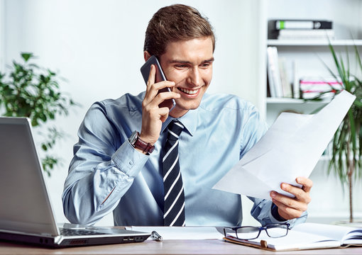 Worker talking on the phone and looks at the documents. Photo of successful manager working with financial data in the office. Business concept