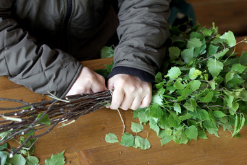 Preparation birch broom for the bath. Man's hands knit fresh branches of a birch tree