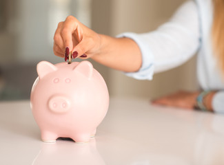 Beautiful young woman hands holding a coin investing in to a piggy bank at home. Business concept.