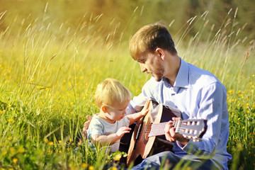 Father teaching his son to play guitar on summer field. Time together dad and son