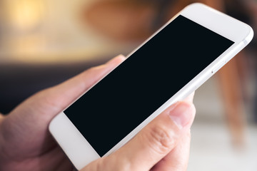 Mockup image of hands holding white mobile phone with blank black desktop screen