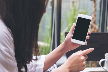 Mockup image of a woman holding and showing white mobile phone with blank black screen in cafe