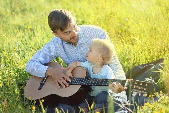 Father teaches his son to play guitar. Smiling and looking at each other. Time together dad and son outdoor