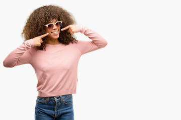 African american woman wearing pink sunglasses smiling confident showing and pointing with fingers teeth and mouth. Health concept.