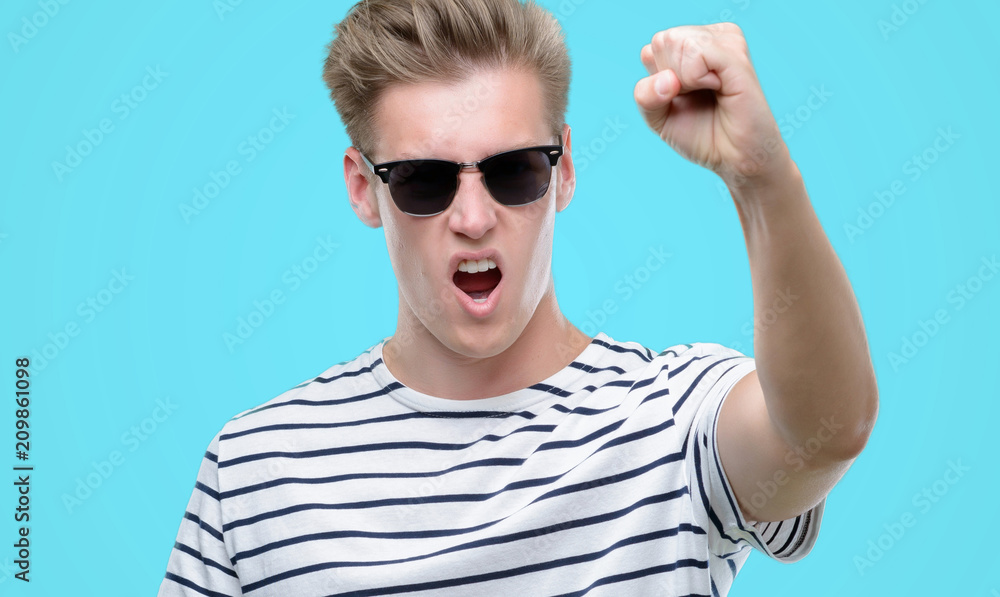 Wall mural Young handsome blond man wearing sunglasess annoyed and frustrated shouting with anger, crazy and yelling with raised hand, anger concept