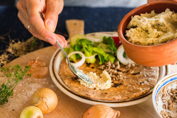 Woman hands holds and spreads dip sauce on garlic naan bread with butter, vegetables salad. Traditional Indian asian plain flatbread made with whole wheat flour. Raw vegan vegetarian healthy food