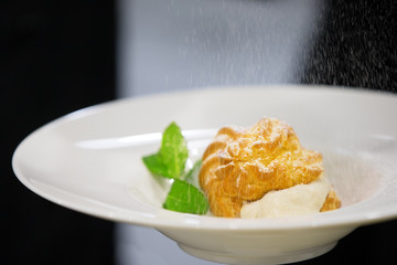Eclair on a plate with mint leaves sprinkled with powdered sugar