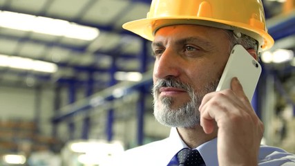 An industrial man engineer with smartphone standing in a factory, making a phone call. - Powered by Adobe