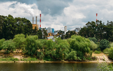Obraz premium Factory next to river emiting plumes of smoke