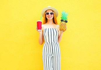 Fashion smiling woman with a pineapple, cup of juice in white striped pants, round hat on yellow...