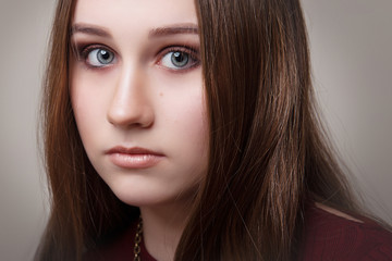 Fototapeta premium A brunette girl with gray eyes and makeup on a gray background close-up.