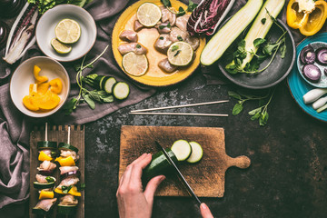 Female hands cut vegetables for Meat skewers making on wooden kitchen table background with chicken pieces, top view. Grill preparation