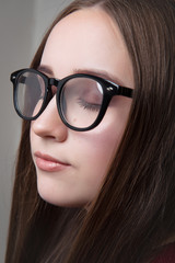 The girl is brown-haired in optical glasses and with makeup on a gray background close-up.
