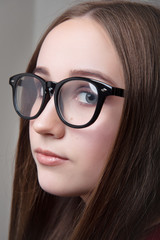 The girl is brown-haired in optical glasses and with makeup on a gray background close-up.