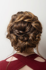 Wedding hairstyle bun on the head of brown-haired women on a gray background close-up rear vie