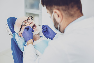 I am ready. Mature man opening mouth while demonstrating his teeth to doctor