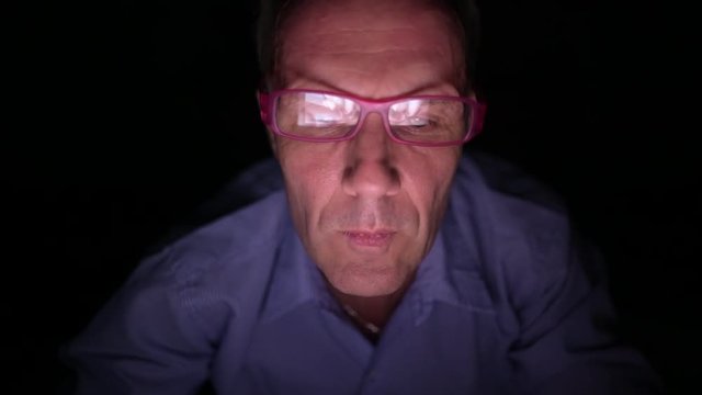 Mature Scandinavian man watching adult videos with digital tablet in dark room