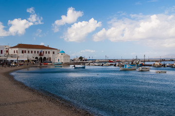 Fototapeta premium Boats at sea port in mykonos, greece. Church and houses in fishing village with nice architecture. Sea beach on blue sky. Summer vacation on mediterranean island. Wanderlust and travelling concept