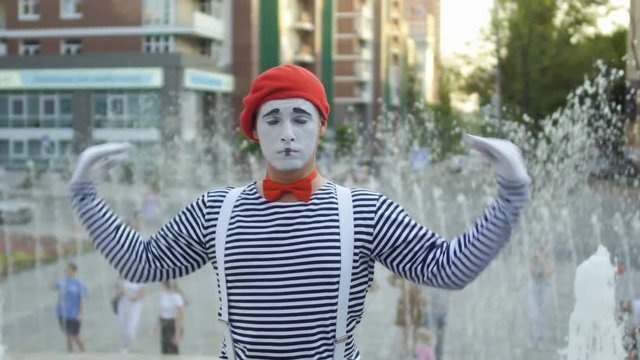 Funny mime conducting and has fun at the fountain background