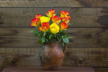 orange and yellow roses in a vase on wooden background