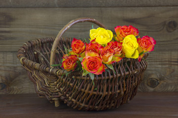 Fototapeta na wymiar orange and yellow roses in a basket on wooden background
